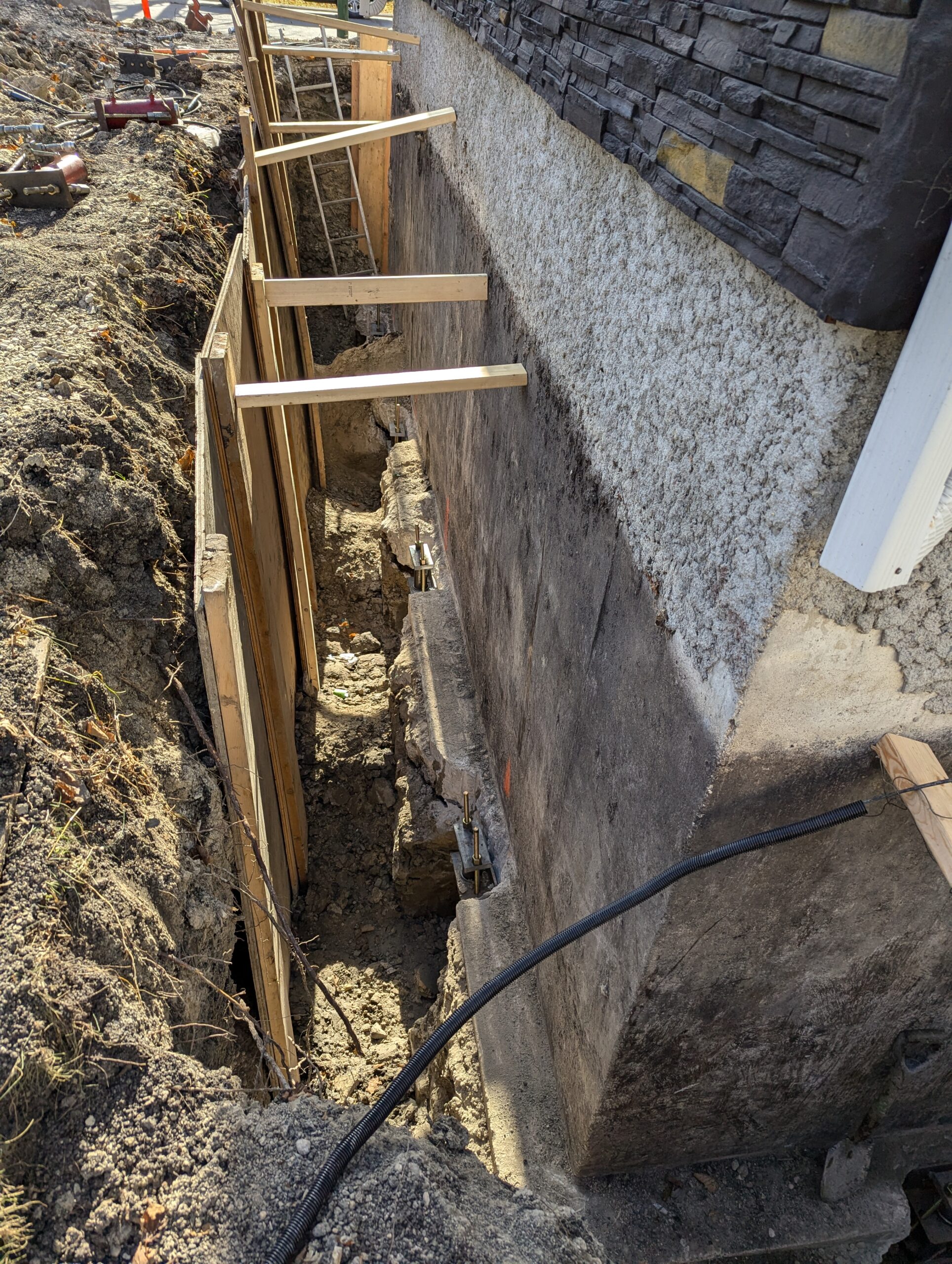 A large metal helical anchor installed in soil, with visible bolts and surrounding excavated earth